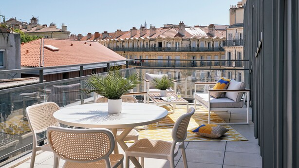 A rooftop terrace with a round table, chairs, potted plants, and a sofa with cushions. - Hôtel LIGO by HappyCulture (Marseille)
