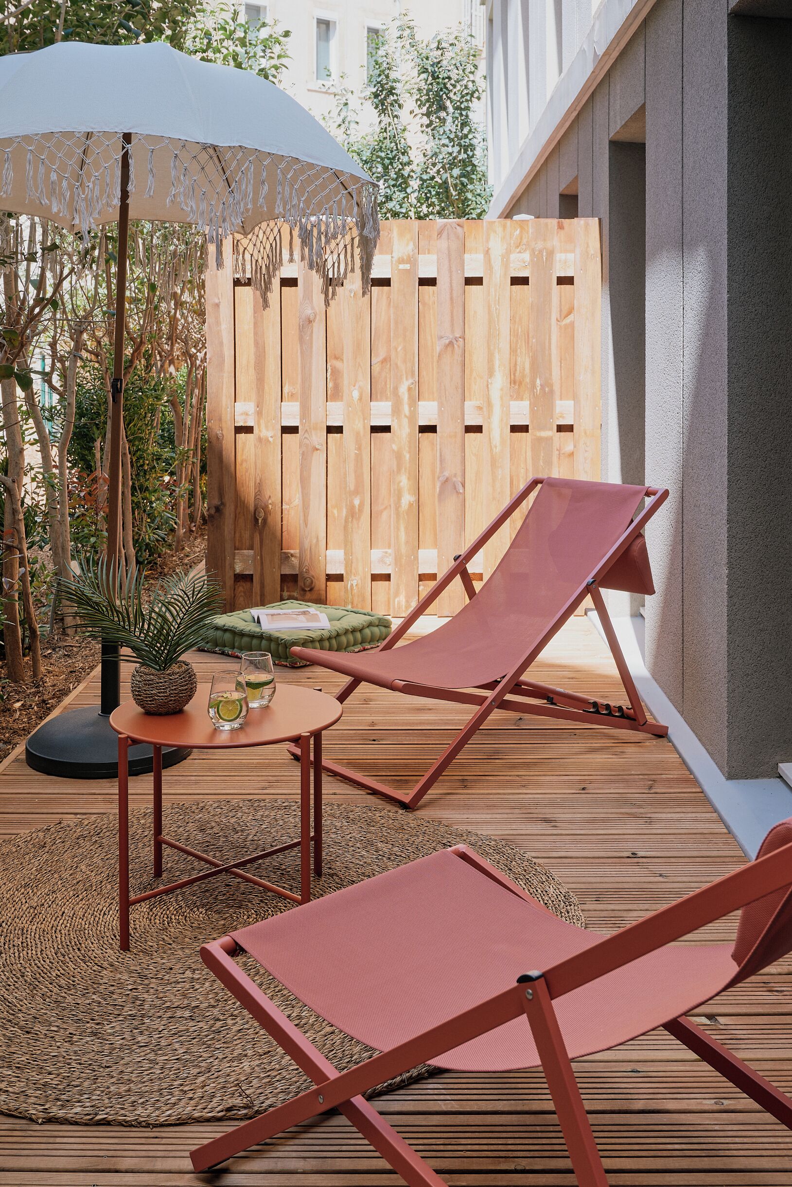 A wooden deck with two red lounge chairs, a white umbrella, and a small table with drinks and a pineapple.