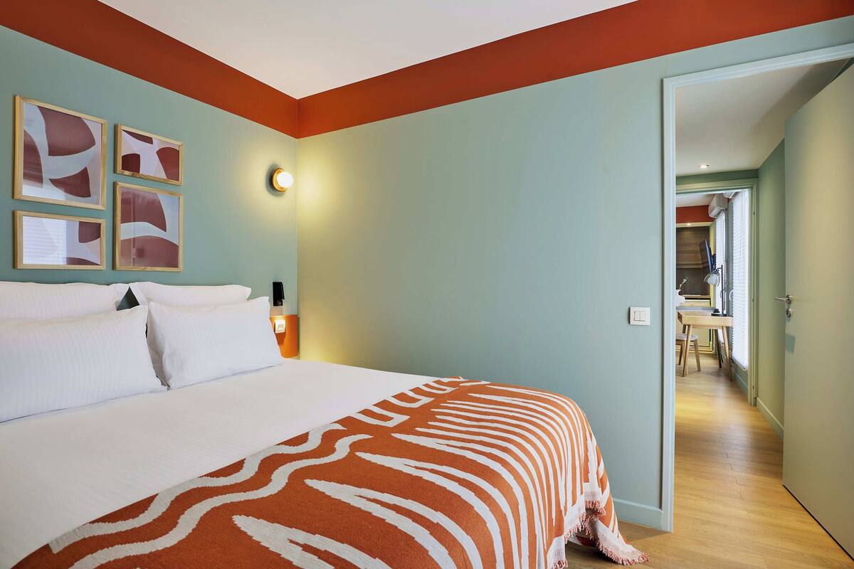Une chambre d’hôtel avec un grand lit, une couverture à motifs zébrés et des œuvres d’art abstraites accrochées aux murs.