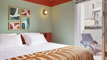 A hotel room with a bed, a balcony with a chair, and abstract wall art.
