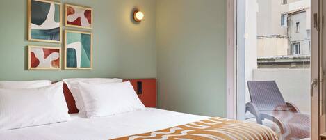 A hotel room with a bed, a balcony with a chair, and abstract wall art.