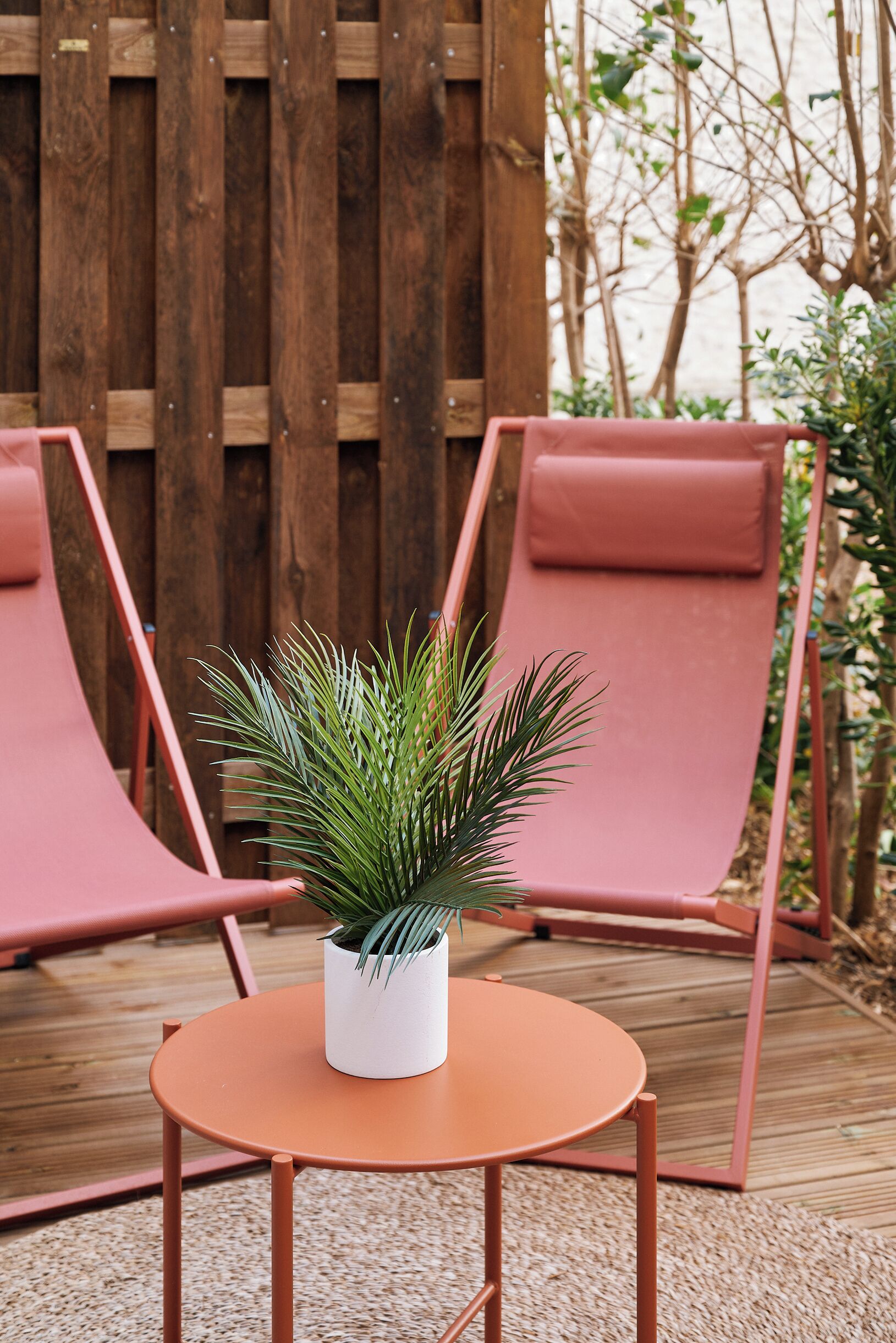 Un terrazza in legno con due poltrone rosa e un tavolino rotondo con una pianta in vaso.
