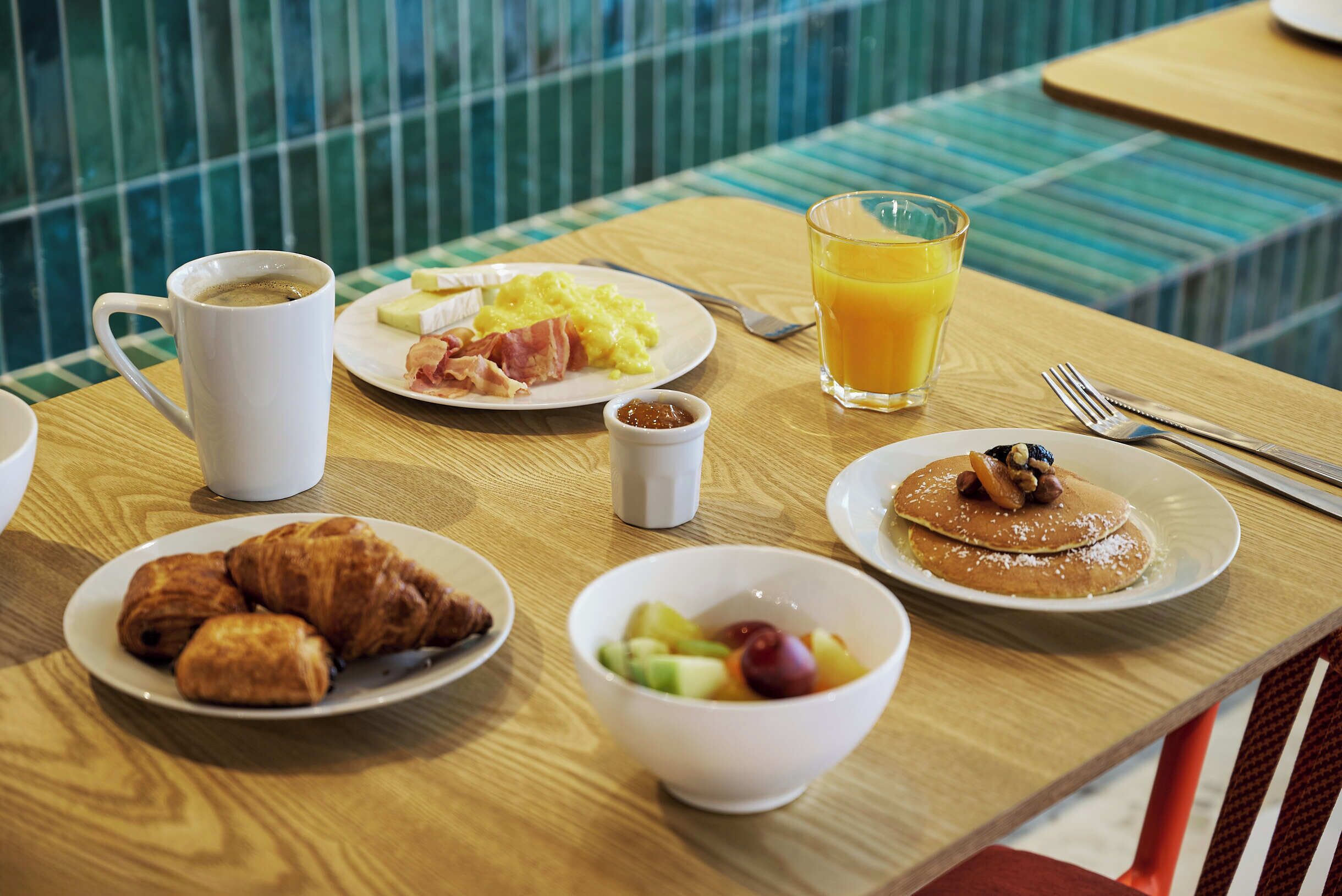 Una tavola imbandita per la colazione con croissant, frutta, pancake e un bicchiere di succo d'arancia.