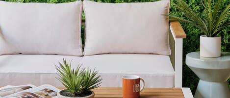 A sofa with cushions, a coffee table with a magazine, a potted plant, and a mug.