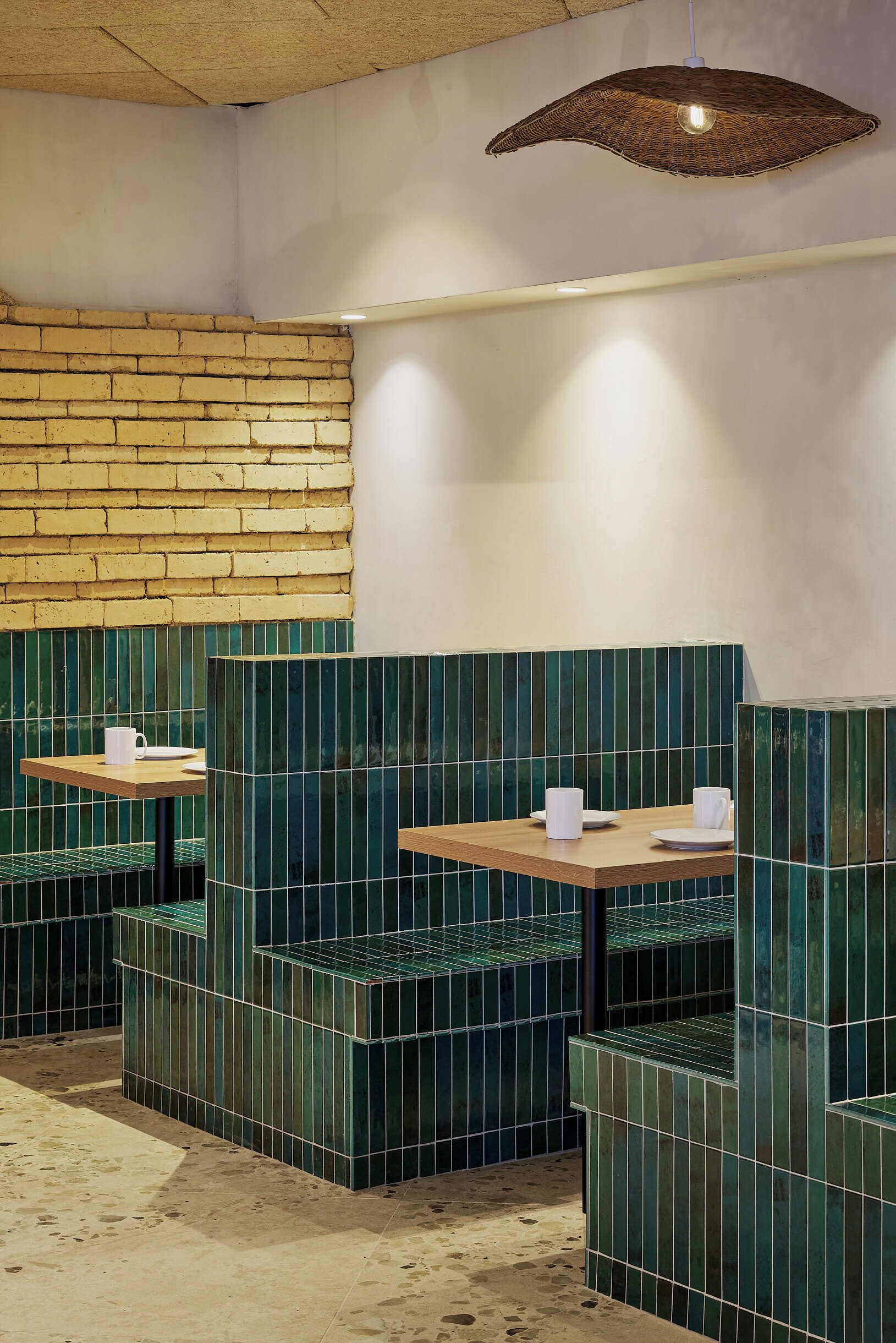 A restaurant interior with brick walls, green-tiled booths, and wooden tables.
