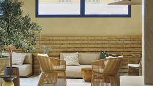 A modern lounge area with wicker furniture, a large plant, and a brick wall. - Hôtel LIGO by HappyCulture (Marseille)