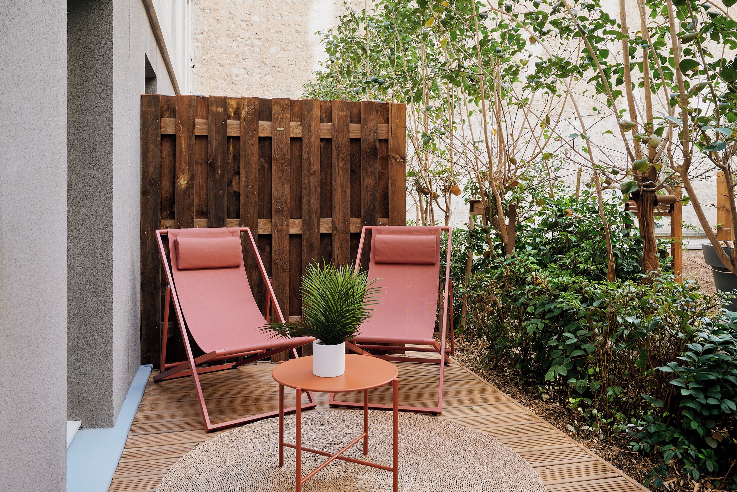 Une terrasse avec deux fauteuils rembourrés, une petite table et un pot de fleurs.