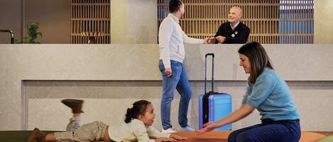 A lobby with a reception desk, a child playing on an ottoman, and a woman interacting with a man.