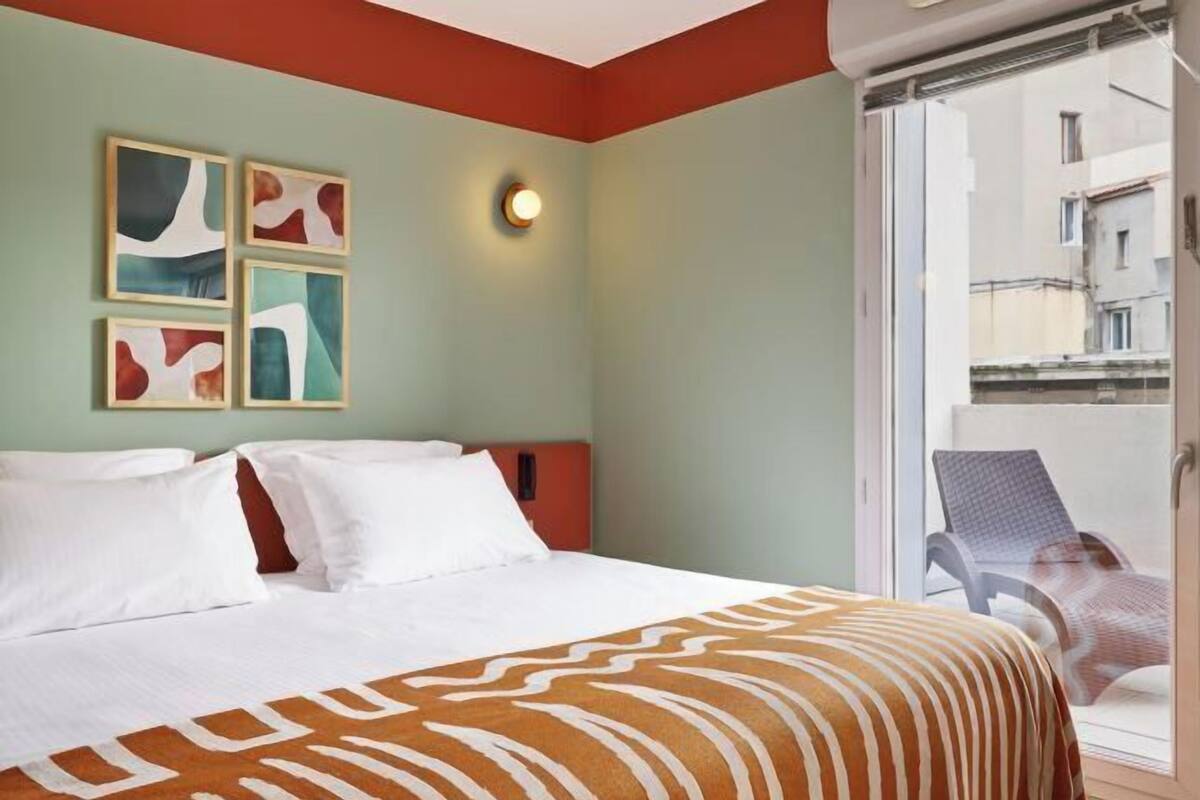 Une chambre d’hôtel avec un lit, une vue sur les immeubles et un balcon avec une chaise.