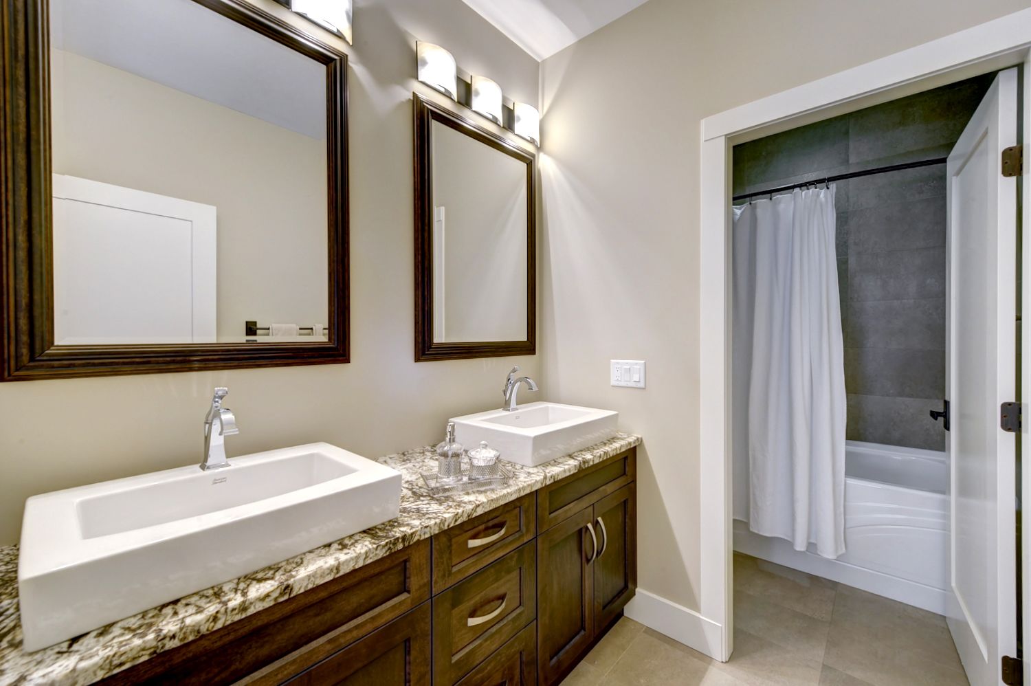 A bathroom with two sinks, a vanity with drawers, a large mirror, and a shower area with a curtain.