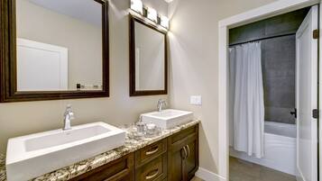 A bathroom with two sinks, a vanity with drawers, a large mirror, and a shower area with a curtain.