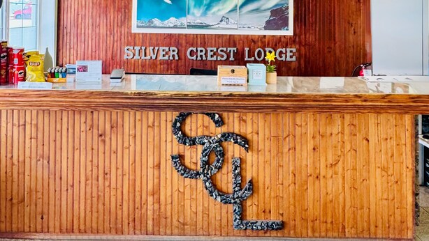 Una recepción en Silver Crest Lodge con un diseño de paneles de madera, una gran foto enmarcada de un paisaje montañoso y un reloj en la pared.