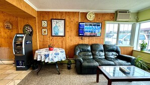 Un hall con paneles de madera, un reloj, un cajero automático, una mesa con mantel floral, un sofá de cuero y una ventana con vista a la calle.