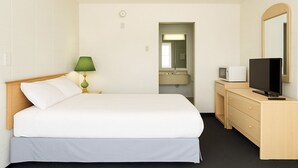 Una habitación de hotel con una cama, una mesita de noche con lámpara, un aparador con televisor y un espejo.