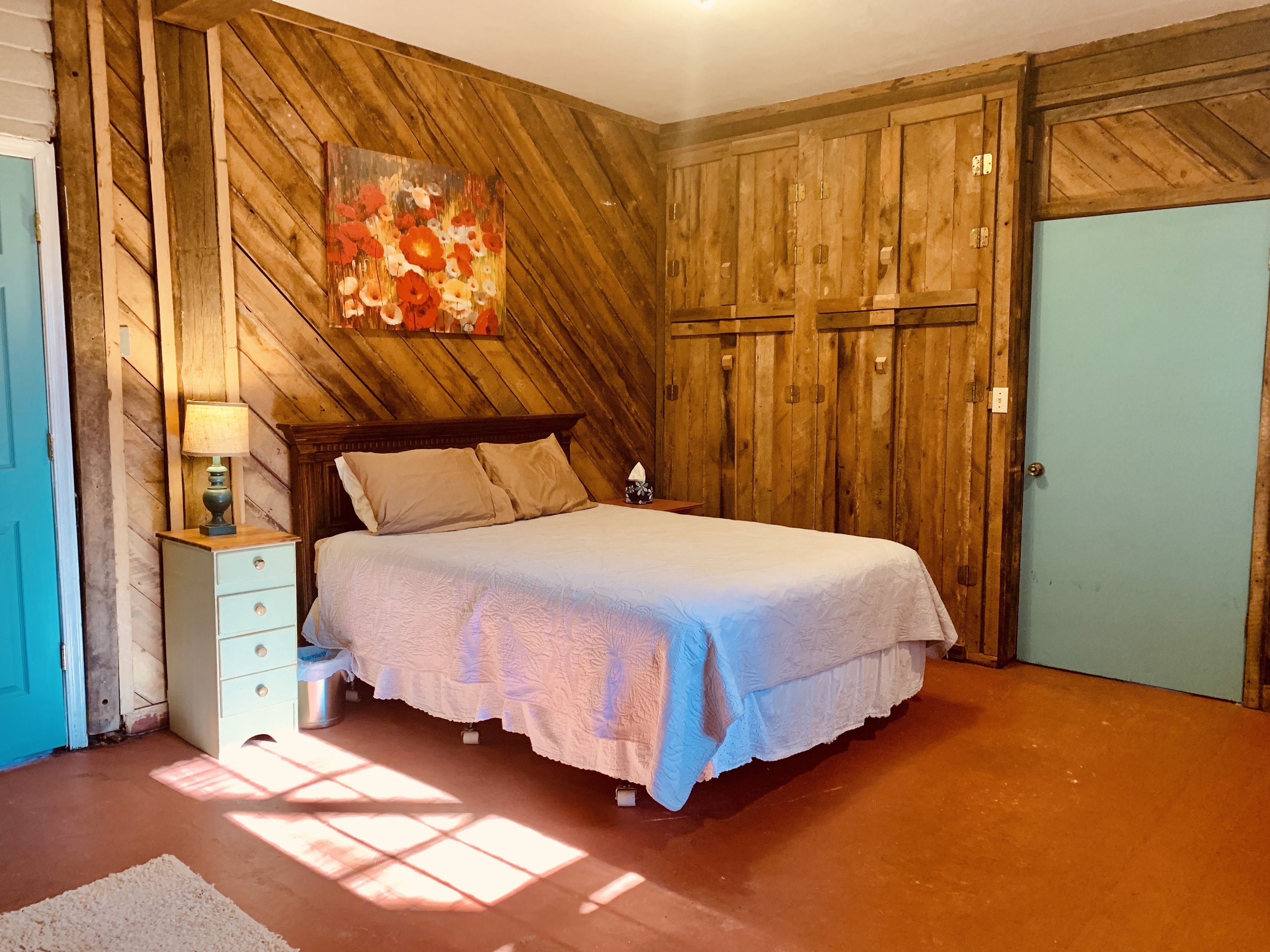 A bedroom with a wooden slat wall, a bed with a white bedspread, a nightstand with a lamp, and a blue door.