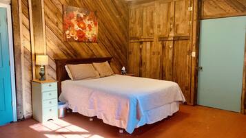 A bedroom with a wooden slat wall, a bed with a white bedspread, a nightstand with a lamp, and a blue door.
