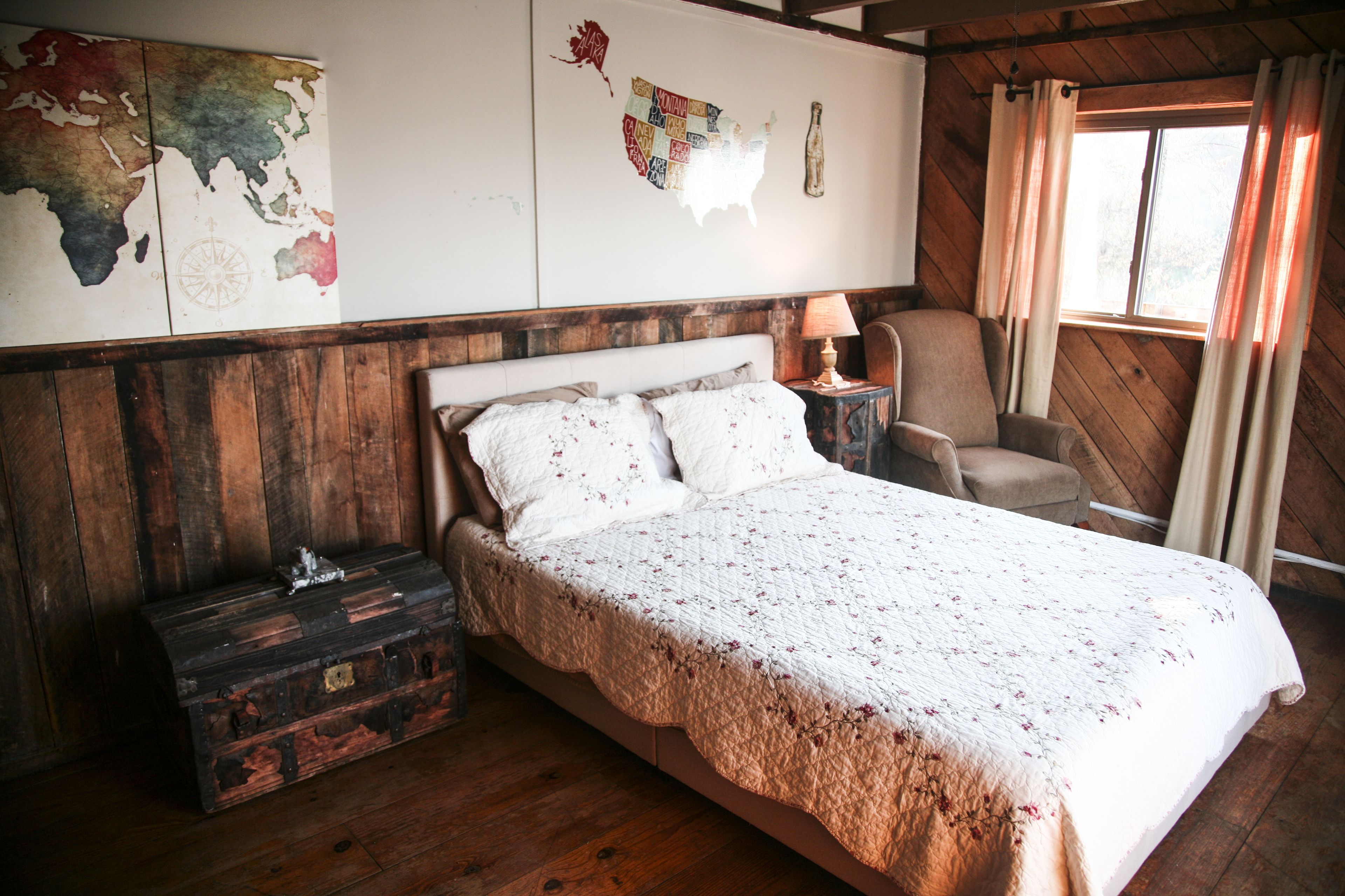 A wooden-paneled room with a bed, a map on the wall, and a window with curtains.