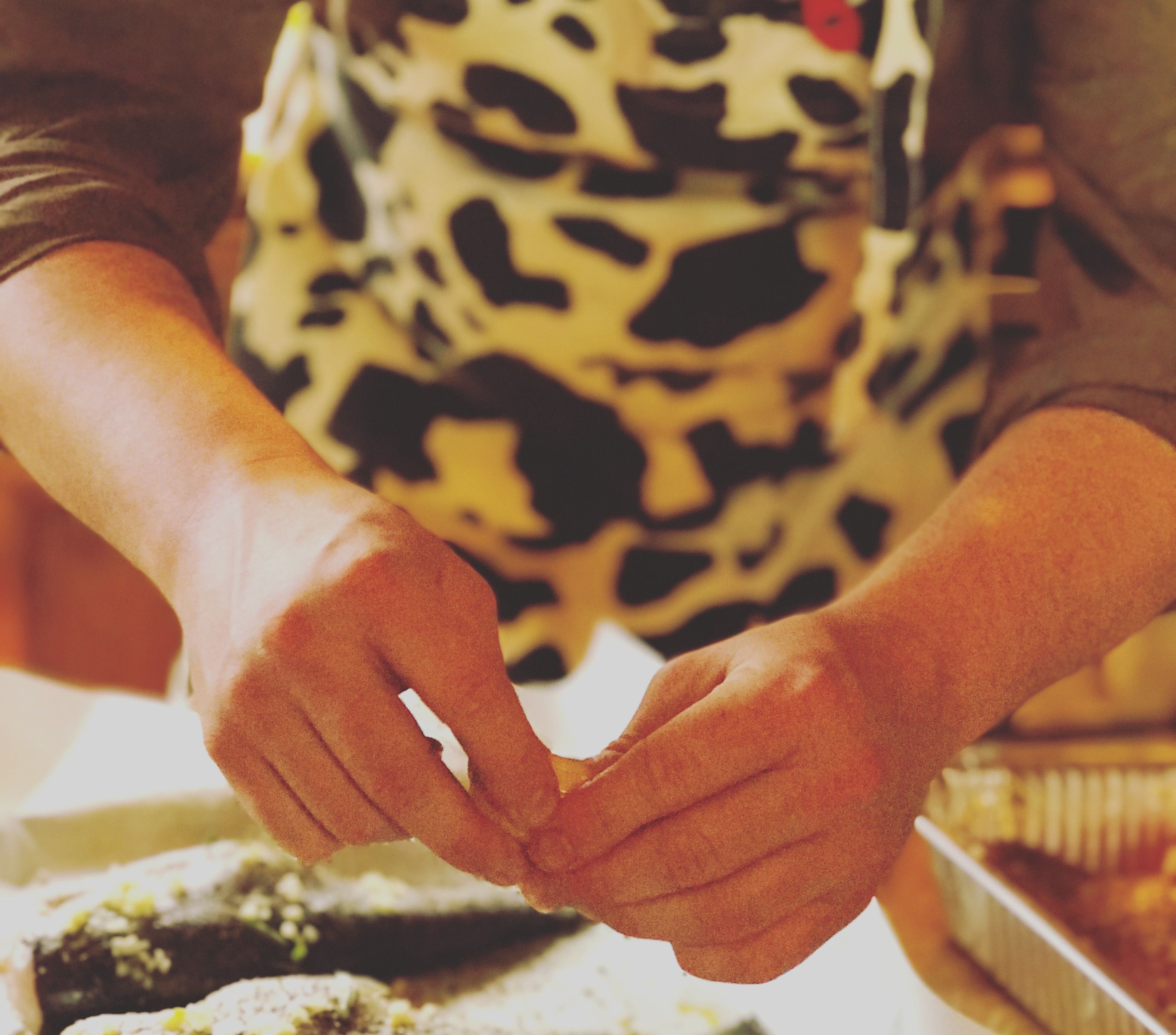 A person wearing a patterned apron, working with dough on a tray.