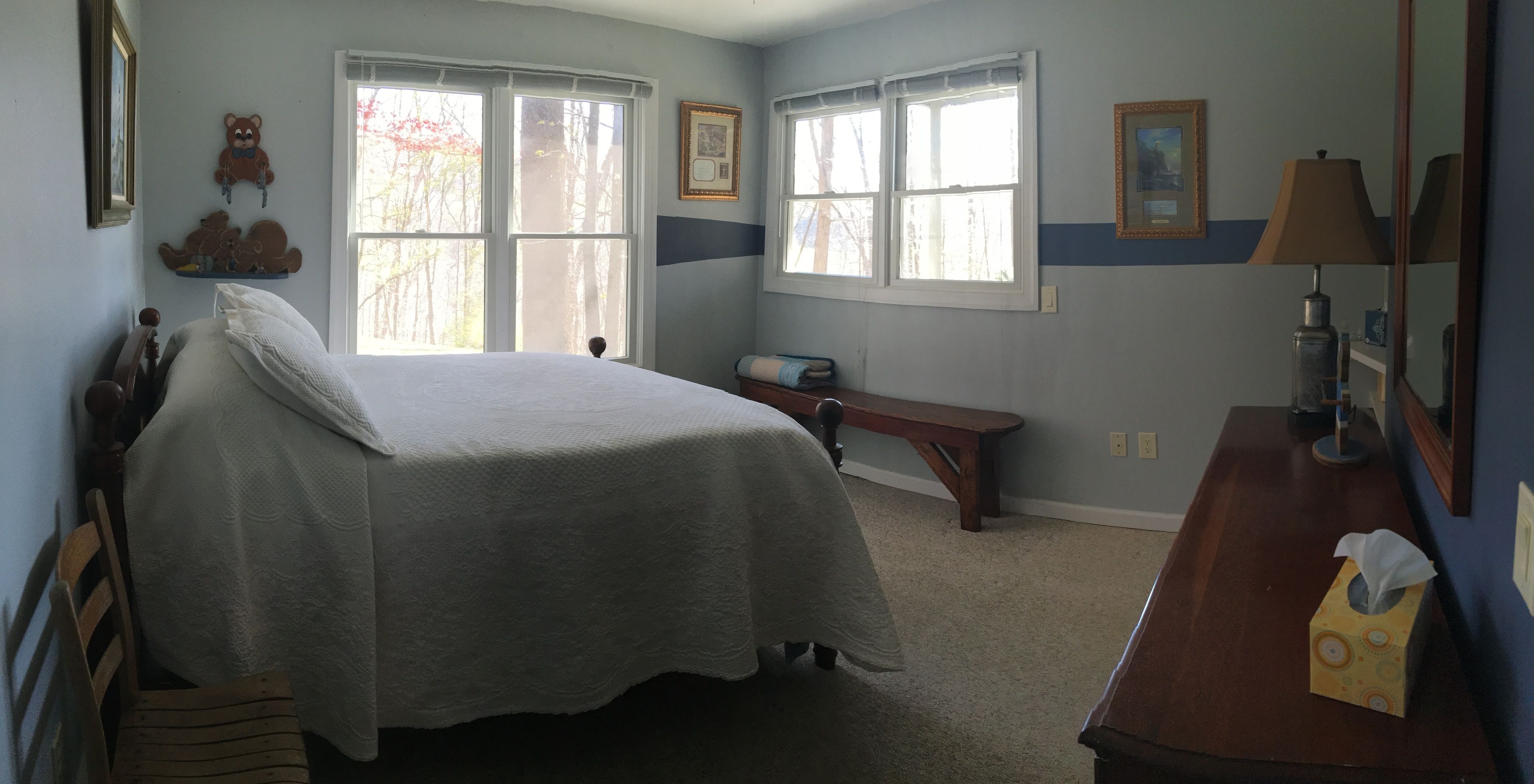 Un dormitorio con cama, escritorio y silla. Hay dos ventanas y una lámpara sobre el escritorio.