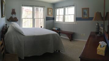 Un dormitorio con cama, escritorio y silla. Hay dos ventanas y una lámpara sobre el escritorio.