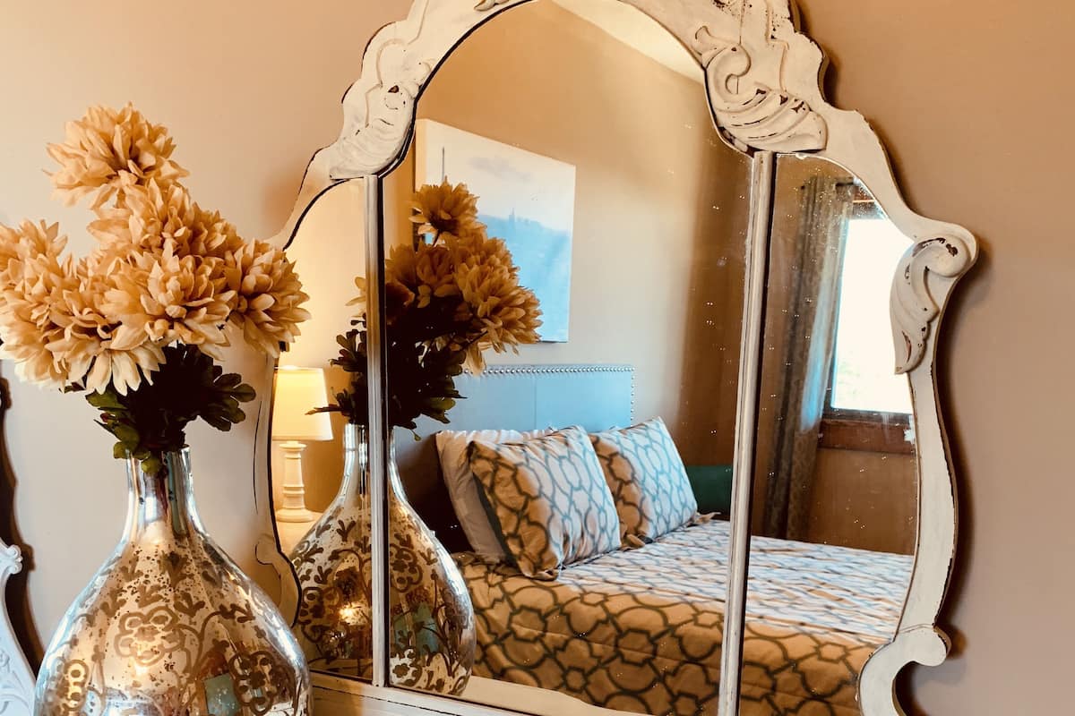 A vintage-style dresser with a mirror, two glass vases with dried flowers, and a small decorative item.