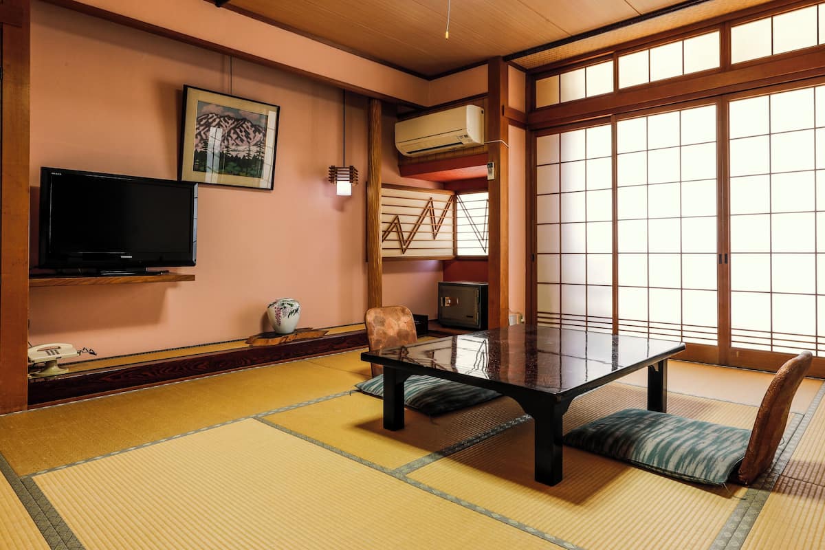 A tatami mat room with a low table, a television, a decorative vase, and a sliding door.