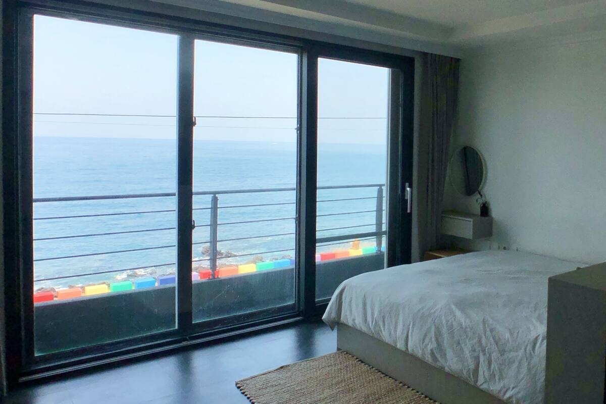 A bedroom with a large sliding glass door leading to a balcony with a view of the sea.