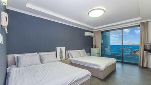Hotellihuone, jossa on kaksi sänkyä, suuri ikkuna, josta on näkymä merelle, kattovalaisin ja puhelin seinässä.