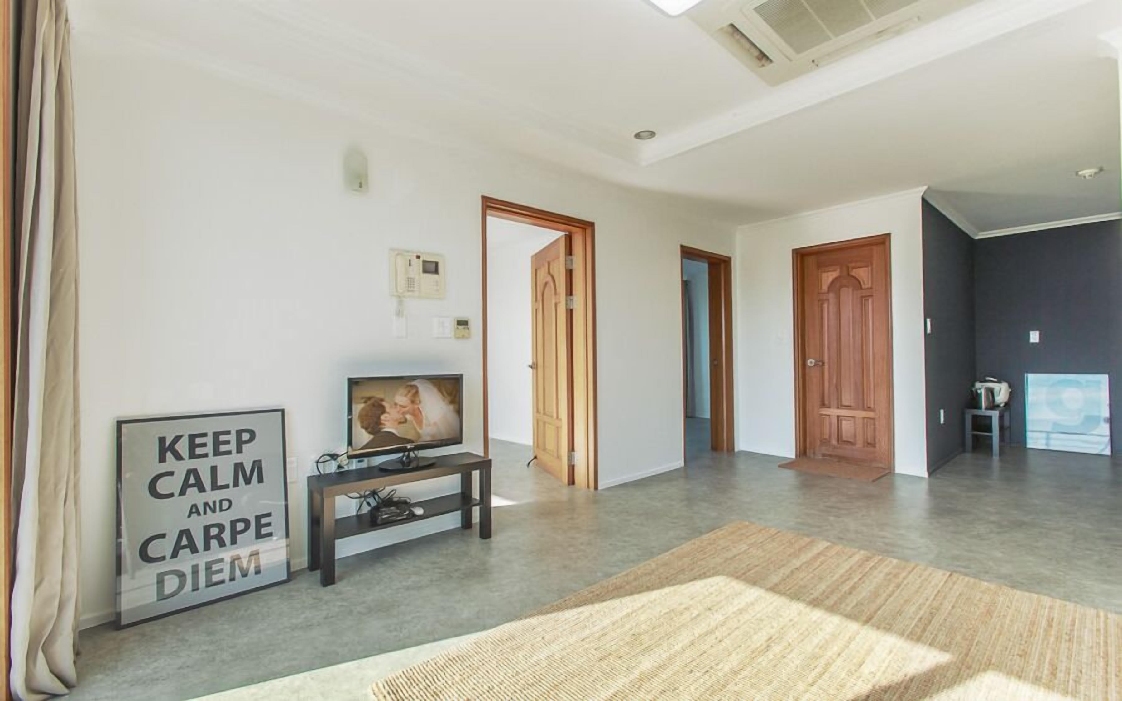 Een ruime woonkamer met een flatscreen-tv, een ingelijste foto en een bord met de tekst 'KEEP CALM AND CARPE DIEM'.
