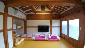 Perinteinen japanilaistyylinen huone, jossa on tatamimatto, seinälle asennettu televisio ja puinen kattorakenne.