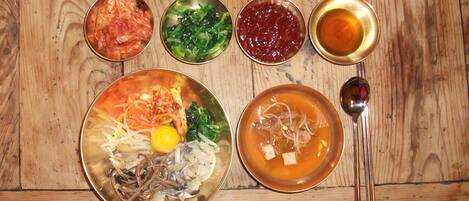 Una mesa de madera con varios platos, incluyendo un bol de sopa, un plato con verduras y varios recipientes pequeños de condimentos.