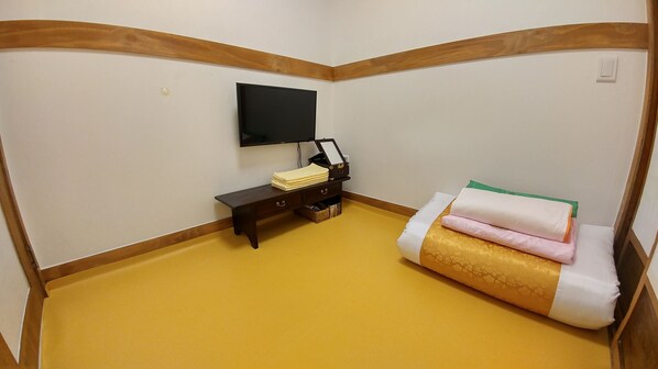 A room with a yellow floor, a wooden bench, a small table with a TV, and a bed with pillows.