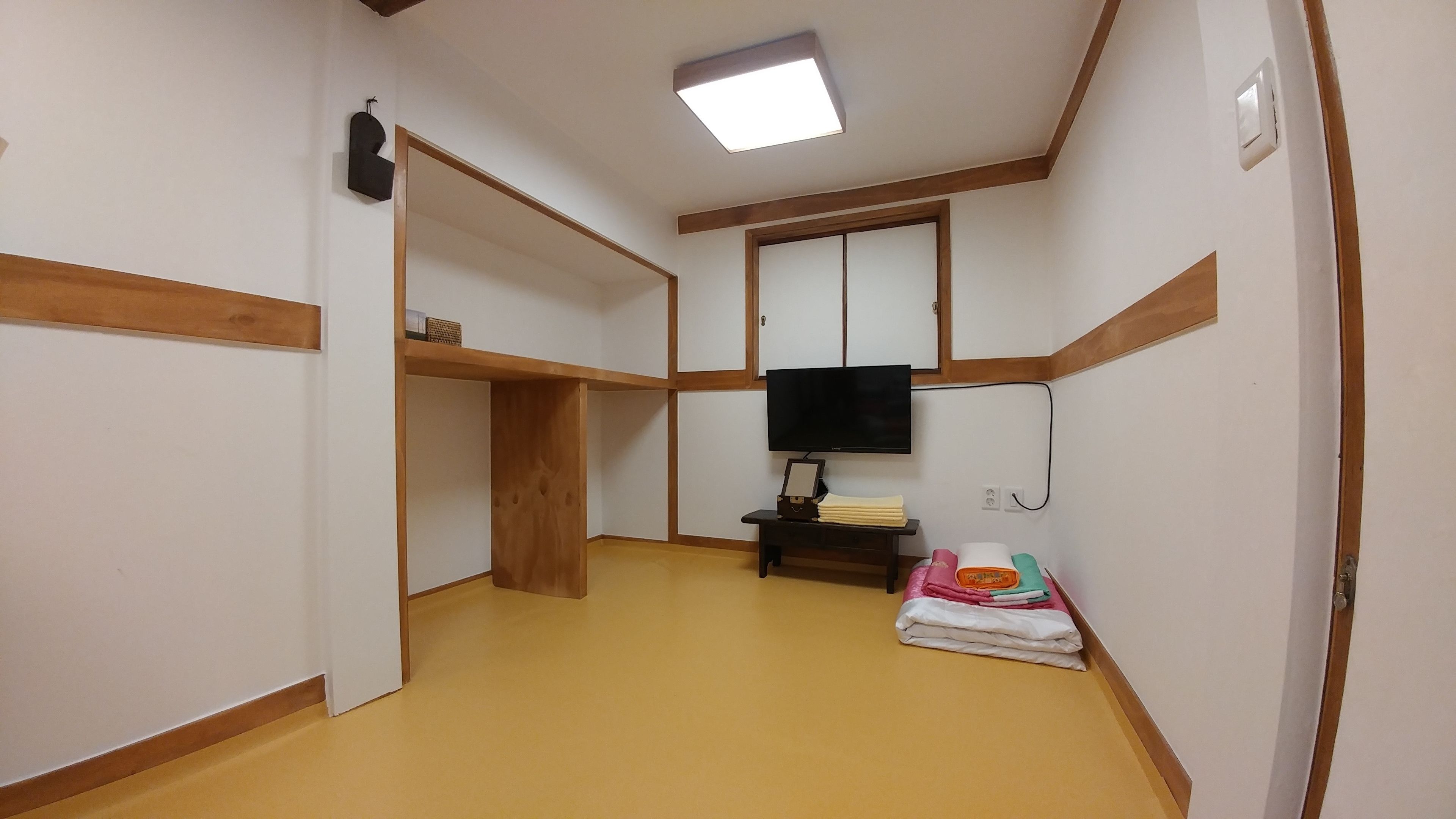A narrow hallway with wooden paneling, a flat-screen TV mounted on the wall, and a small table with folded blankets.