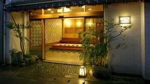 A traditional Japanese building with a wooden entrance, tiled floor, and a small garden area with plants and a lantern. - Sinonomesou (Toyooka)