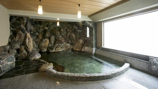 A stone-walled hot tub with a clear water feature, wooden ceiling beams, and a window on the right side. - Sinonomesou (Toyooka)