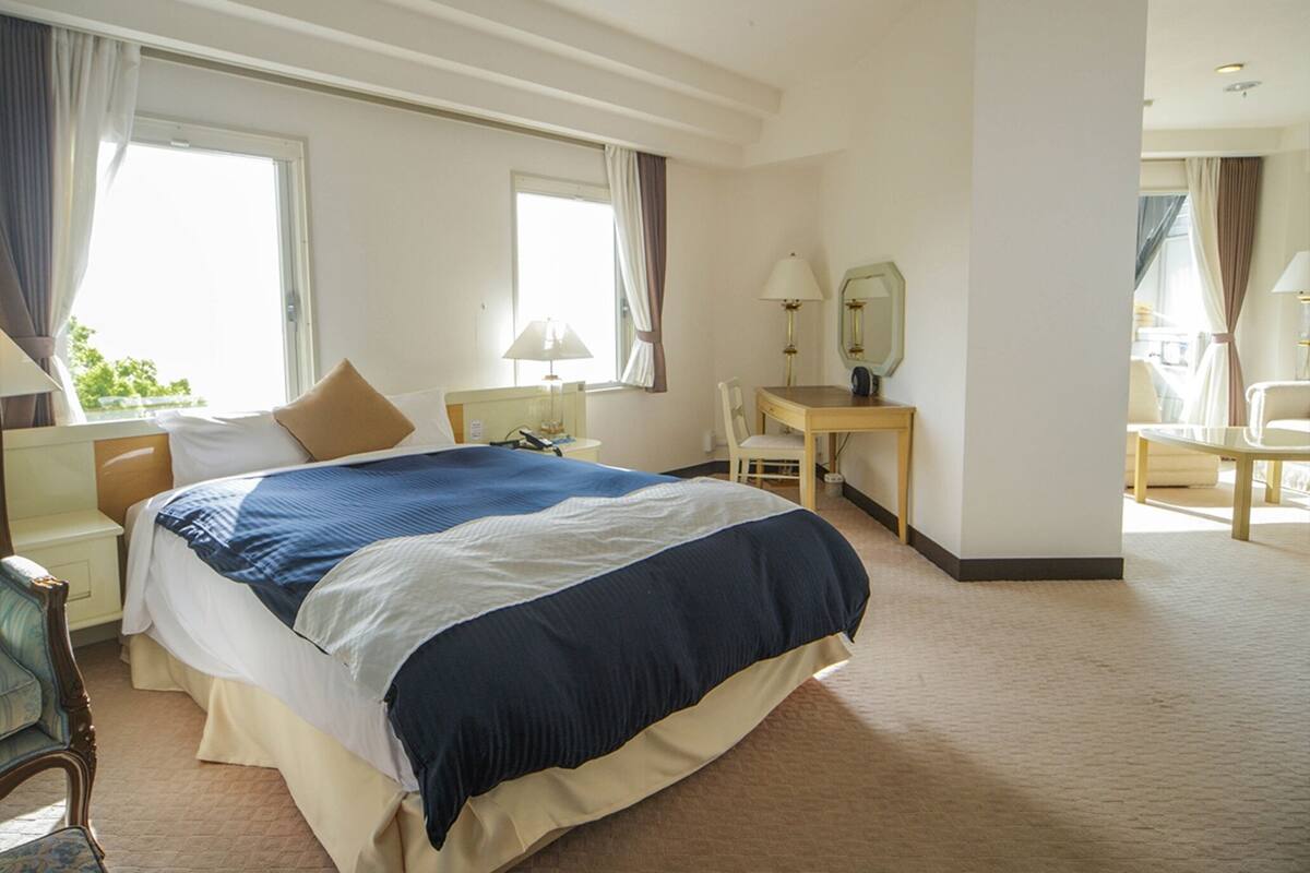 A hotel room with a large bed, a desk, a chair, and a mirror.
