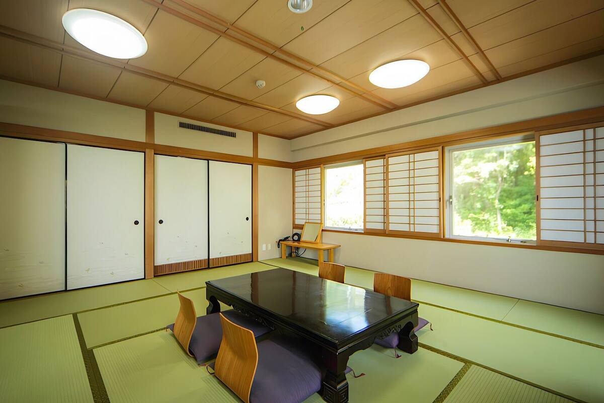 A traditional Japanese room with tatami flooring, sliding doors, a low table, and a view of greenery.