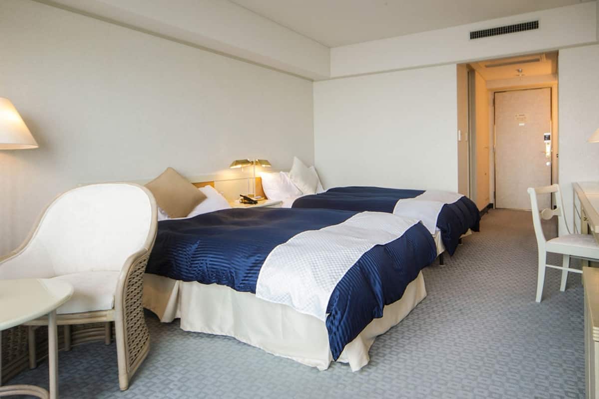 A hotel room with two beds, a chair, a desk, and a door.