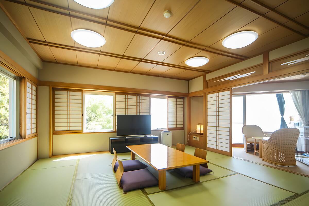 A traditional Japanese room with tatami flooring, a low table, cushions, a television, and sliding doors.