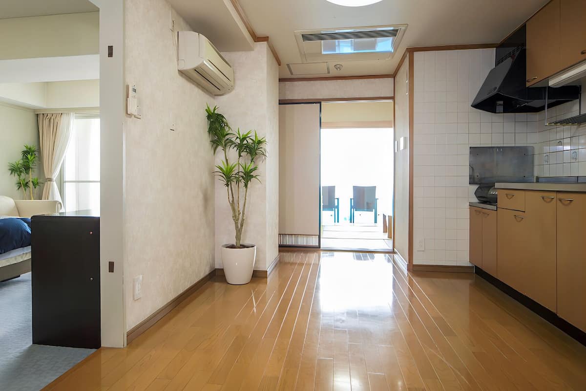 A modern hotel room with a bed, a potted plant, a kitchenette, and a view of the outside.