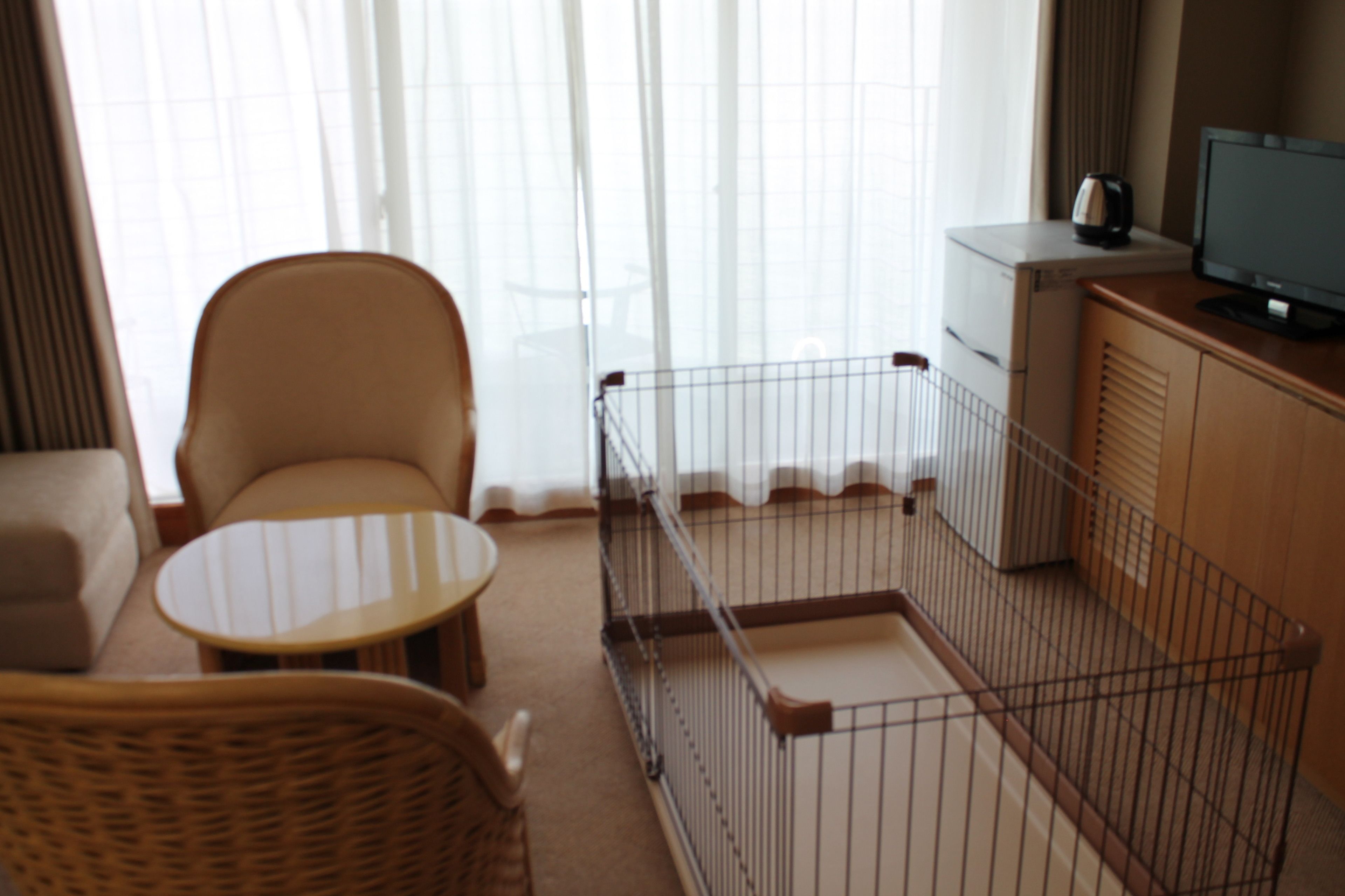 A hotel room with a wicker chair, a small round table, a television on a wooden cabinet, and a metal crib.