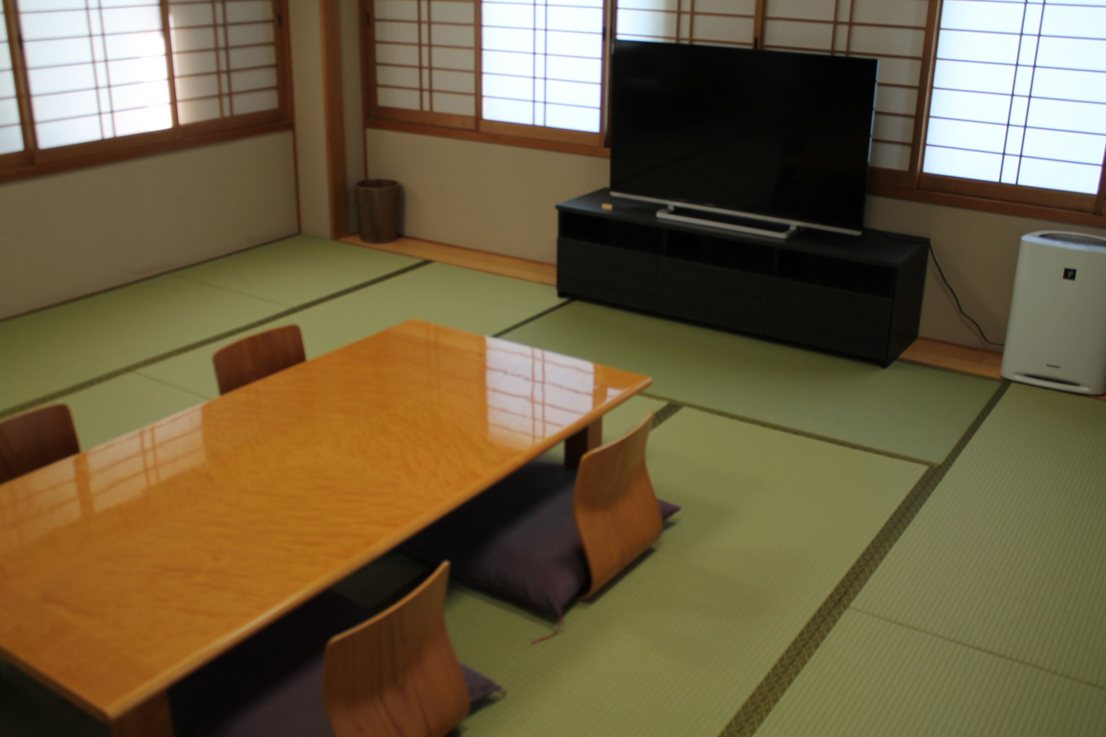Um quarto japonês tradicional com tatames, uma mesa de madeira e uma televisão sobre um suporte.