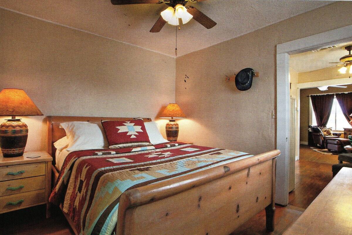 Een slaapkamer met een houten bed, twee bedlampen, een plafondventilator en uitzicht op een andere kamer.