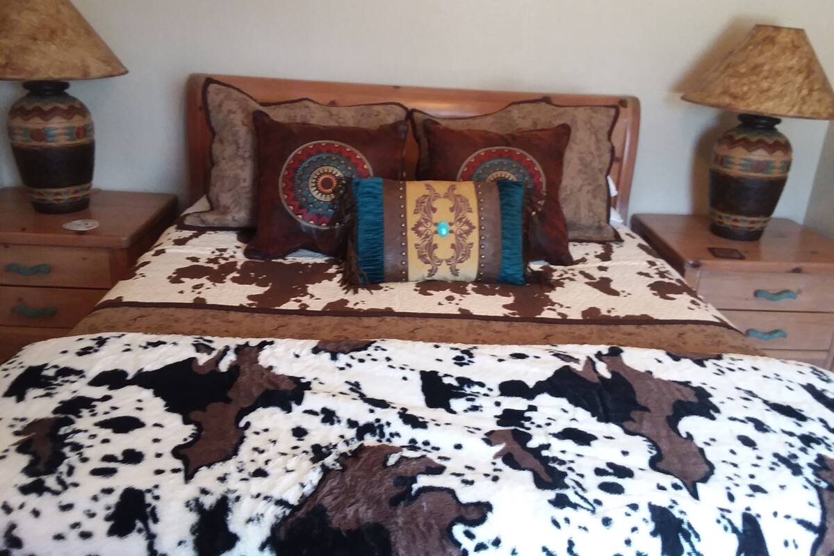 Een bed met een koeienhuiddeken, twee sierkussens en twee nachtkastjes met lampen.