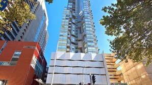 Un bâtiment moderne à la façade géométrique originale, entouré d’autres immeubles de grande hauteur et surplombant un ciel d’un bleu éclatant.