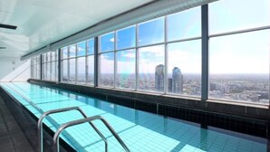 Une longue piscine intérieure avec de grandes baies vitrées offrant une vue sur la ville.