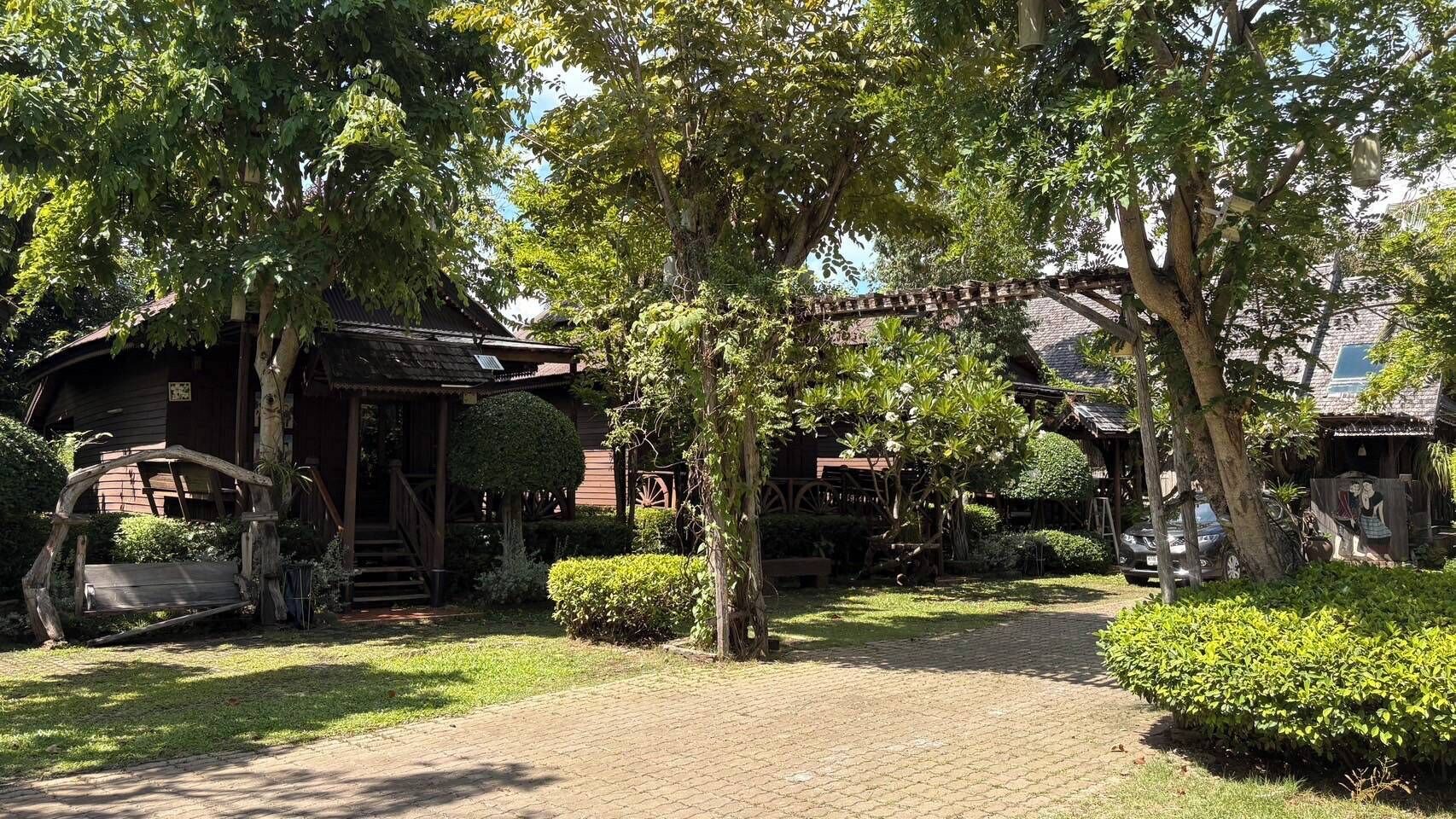 A rustic wooden building with a porch and steps, surrounded by lush greenery and a cobblestone path.