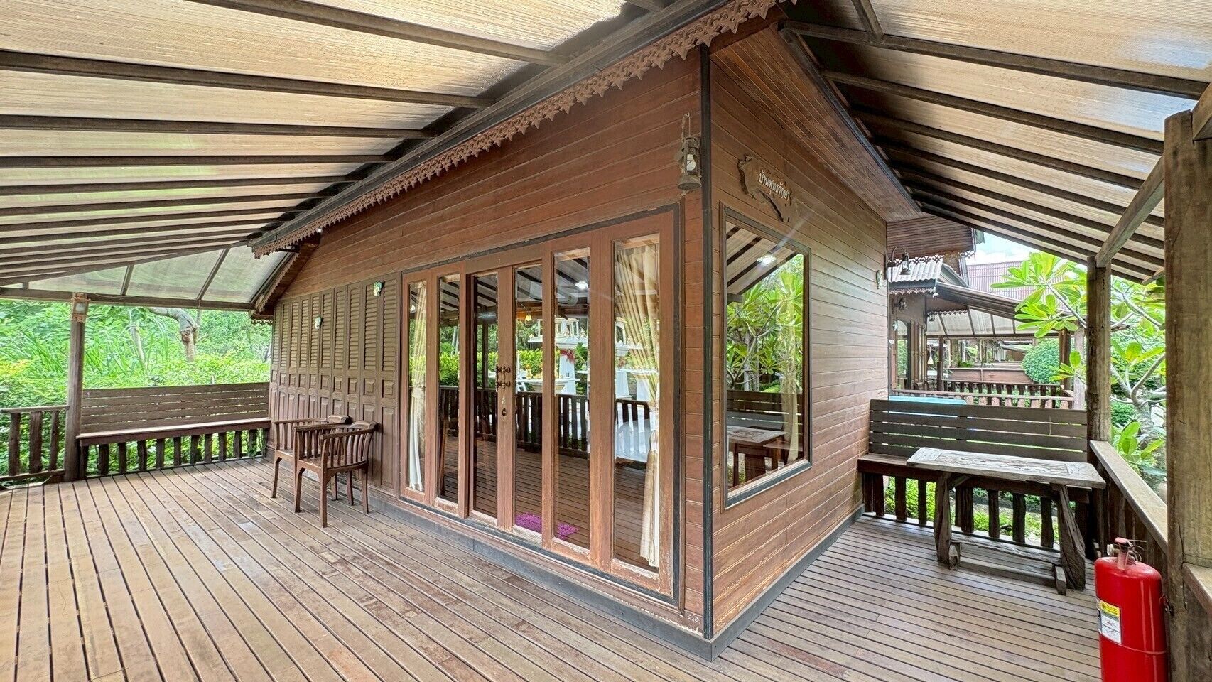 A wooden cabin with a covered porch, large windows, and a fire extinguisher on the deck.