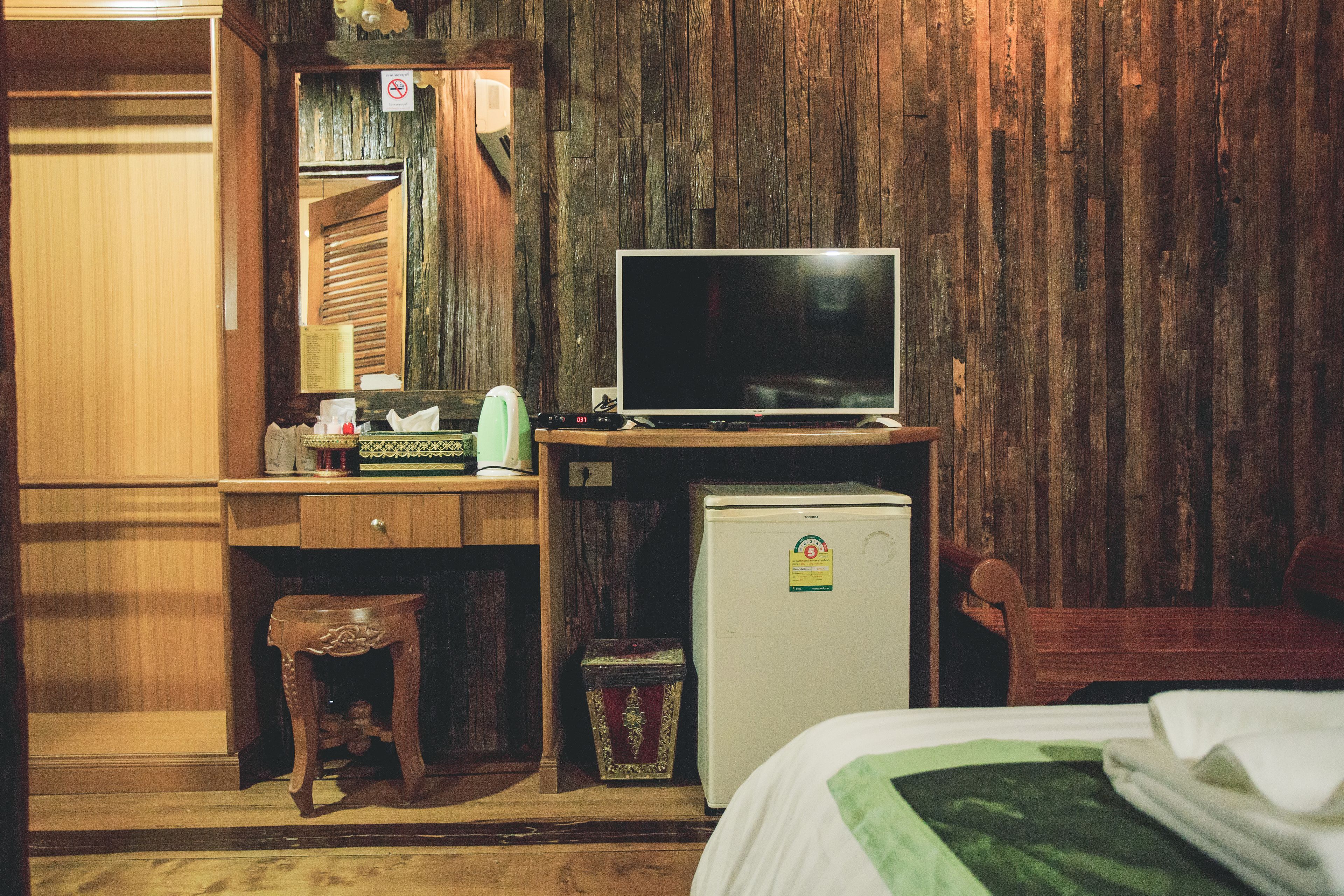 A compact room with a wooden desk, a television, a small refrigerator, and a bed.