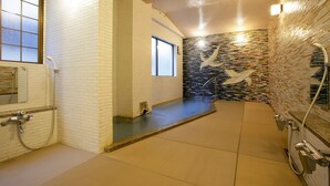 A modern bathroom with a tiled floor, a shower area, and a decorative wall with a mosaic pattern. - Sento Ryokan (Toyooka)